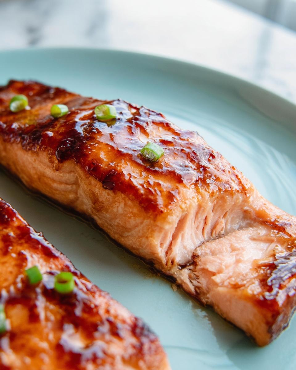 Close-up of a perfectly cooked Miso Glazed Broiled Salmon fillet, glistening with sauce and topped with green onions.