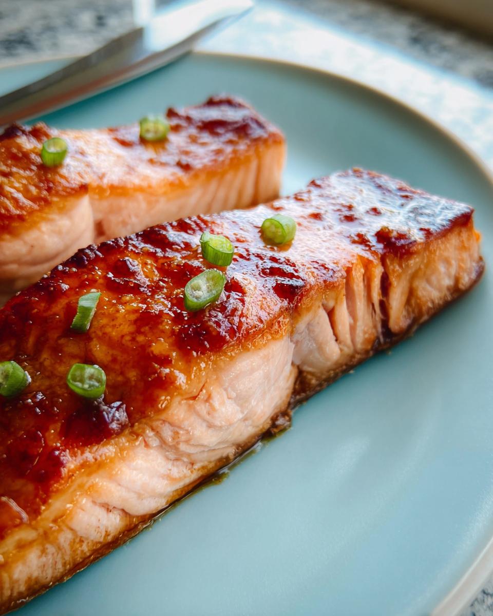 Two perfectly cooked fillets of Miso Glazed Broiled Salmon topped with sliced green onions on a light blue plate.
