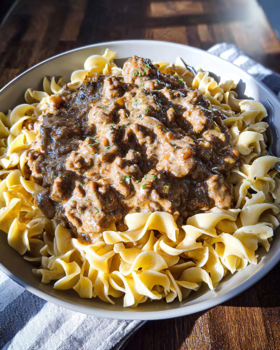 A close-up bowl of creamy One Pot Ground Beef Stroganoff served over wide egg noodles, garnished with herbs.