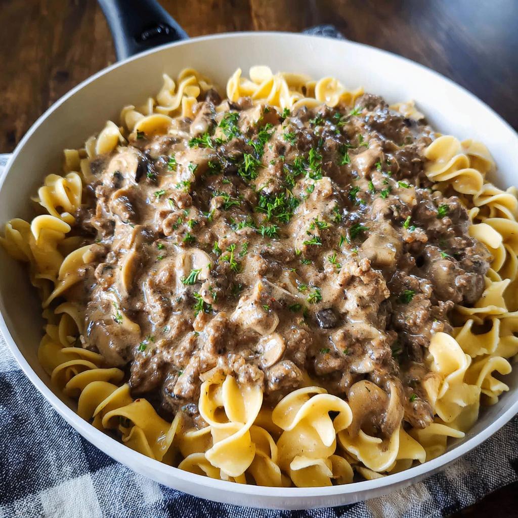 A close-up of creamy One Pot Ground Beef Stroganoff served over egg noodles in a white skillet.