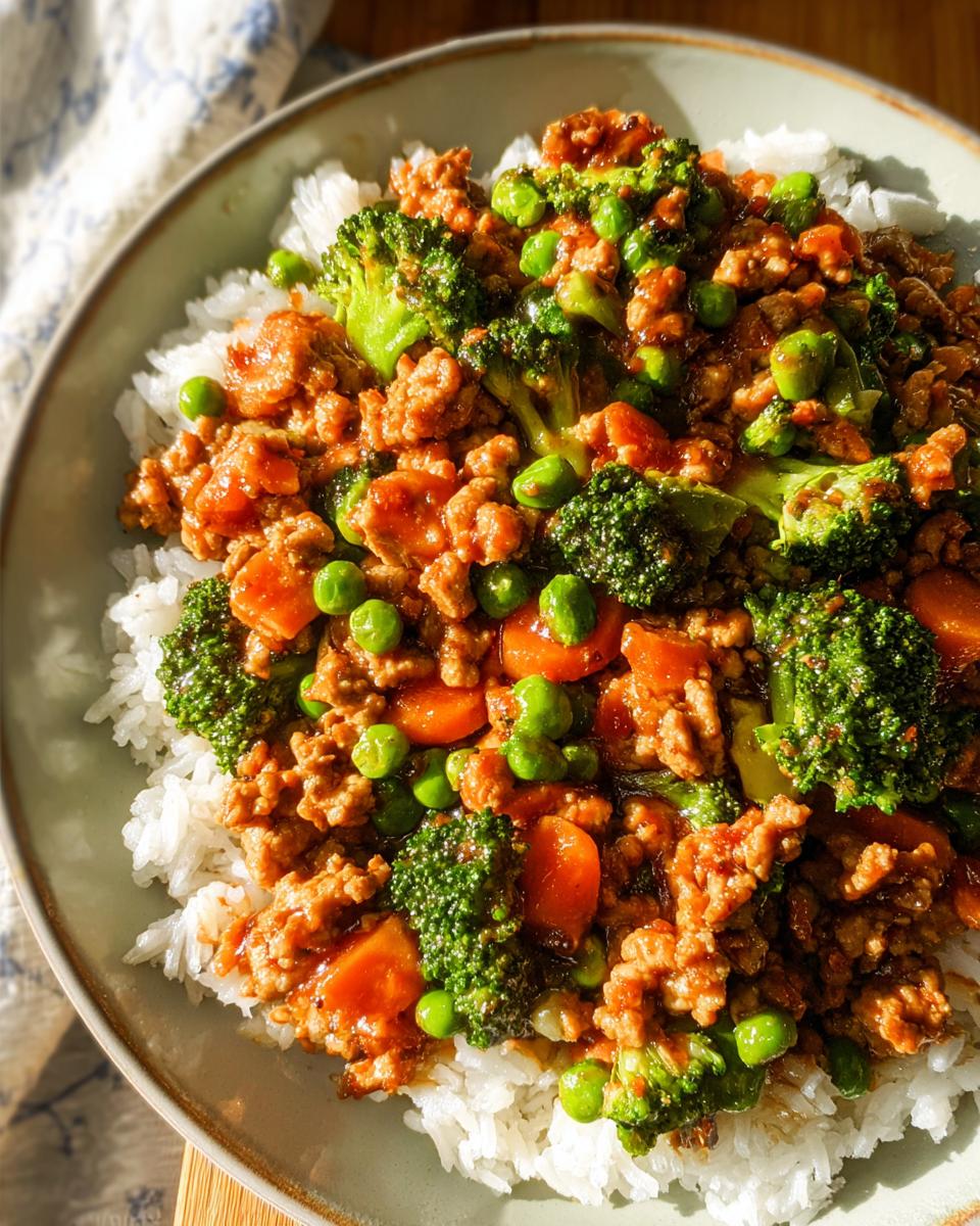 Close-up of a Teriyaki Ground Turkey Bowl featuring ground turkey, broccoli, peas, and carrots served over white rice.