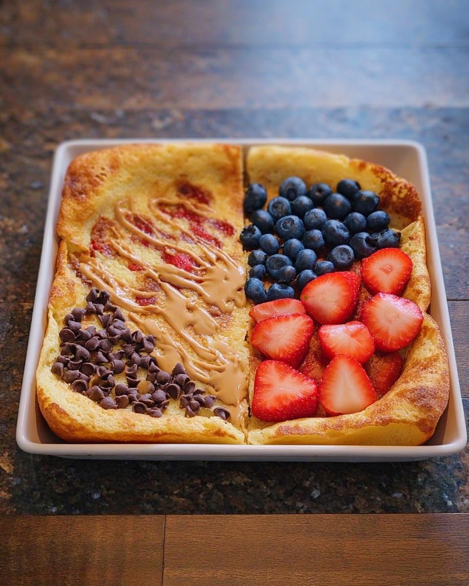 A Dutch baby pancake divided into sections, topped with peanut butter, chocolate chips, blueberries, and strawberries. A perfect 10-ingredient breakfast idea.