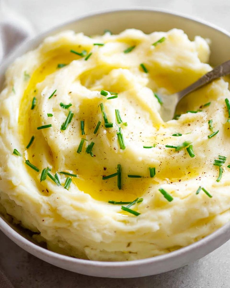Close-up of creamy 12-Ingredient Mashed Potatoes topped with melted butter and fresh chives.