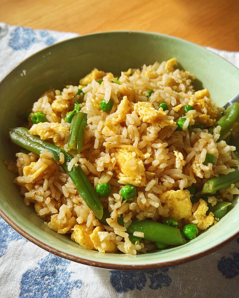 A bowl of 7-ingredient egg fried rice, featuring scrambled egg pieces, green peas, and green beans mixed with rice.