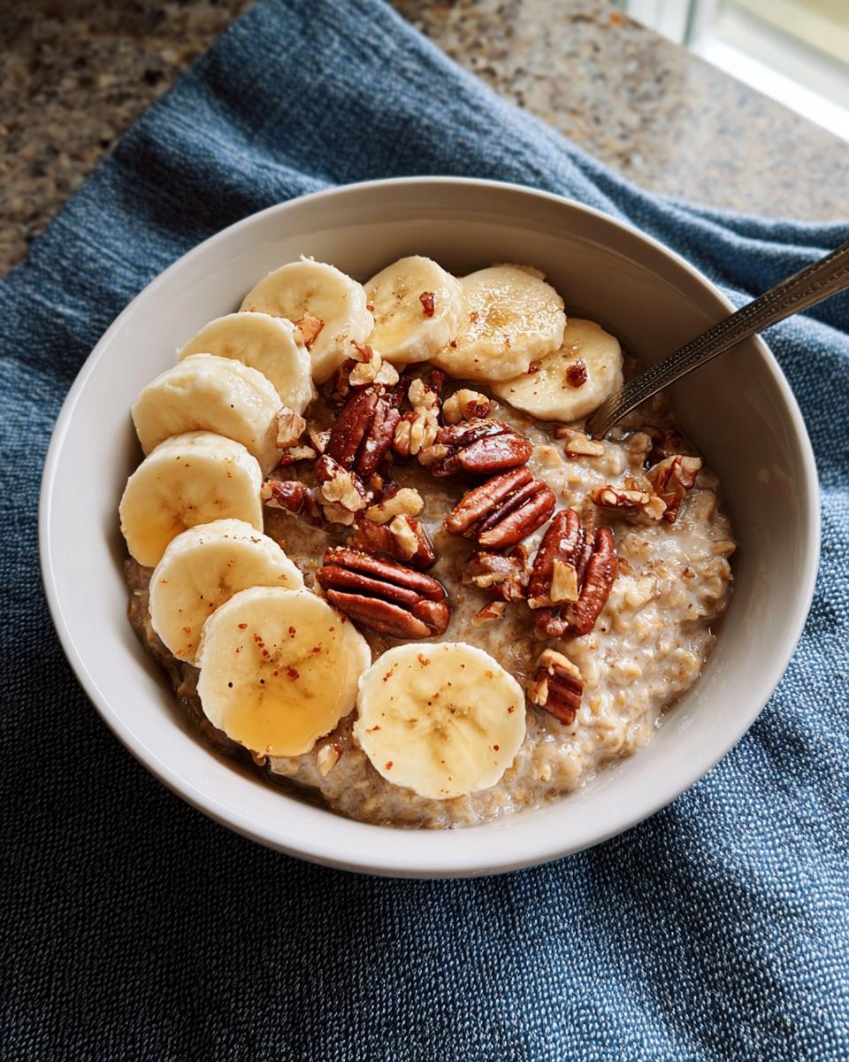 A bowl of warm oatmeal topped with sliced bananas, pecans, and a drizzle of honey, perfect for busy weeknights.