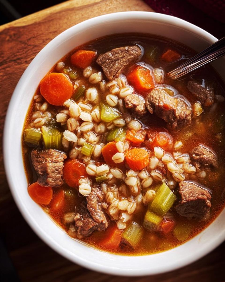 A close-up of a bowl of hearty beef barley soup, featuring tender beef chunks, carrots, celery, and barley.