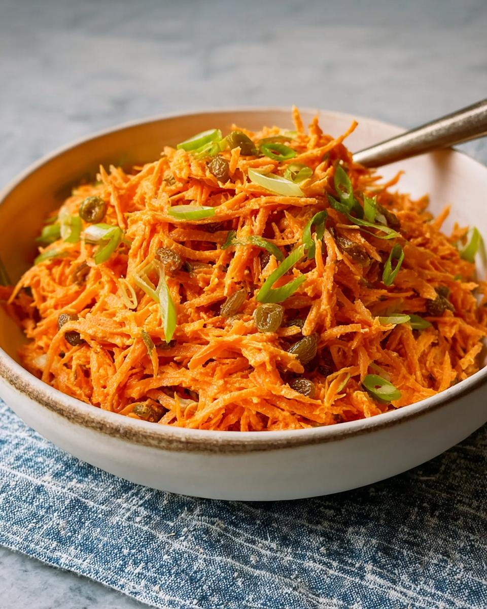 A vibrant bowl of shredded carrot salad with raisins and green onions, perfect for quick veggie sides recipes.