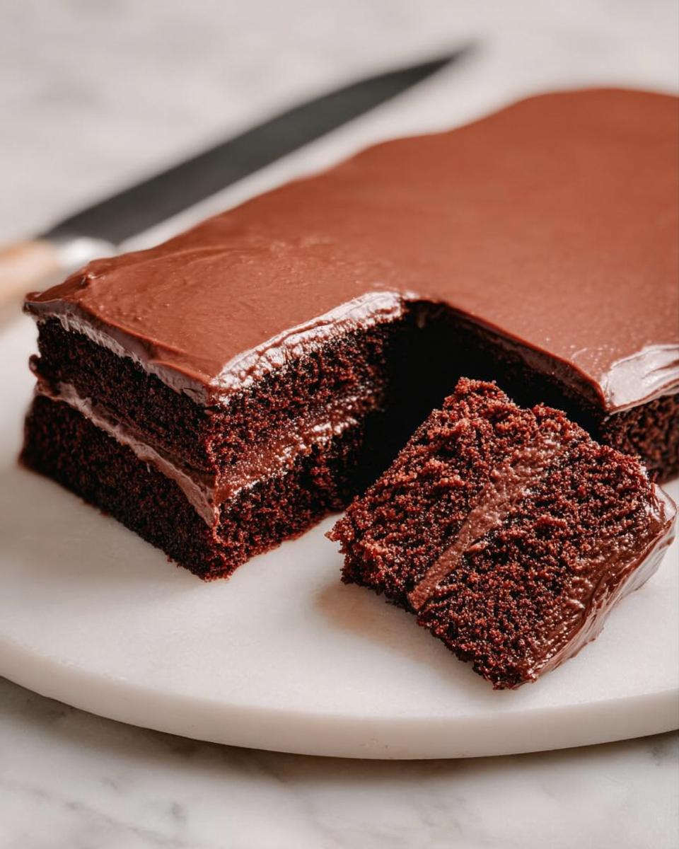 A slice of rich chocolate cake with smooth frosting, showcasing layers of moist cake and creamy filling. Perfect for cake ideas recipes.