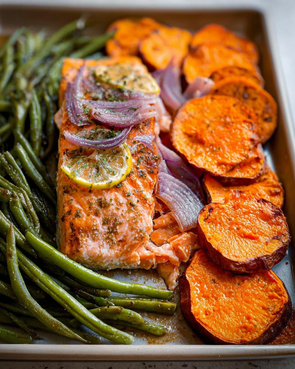 A delicious and healthy sheet pan meal prep featuring a fillet of salmon, roasted sweet potato slices, and green beans.