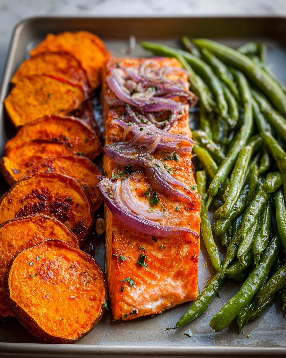 A perfectly cooked salmon fillet with red onion and herbs, served with roasted sweet potato slices and green beans for a healthy meal prep.