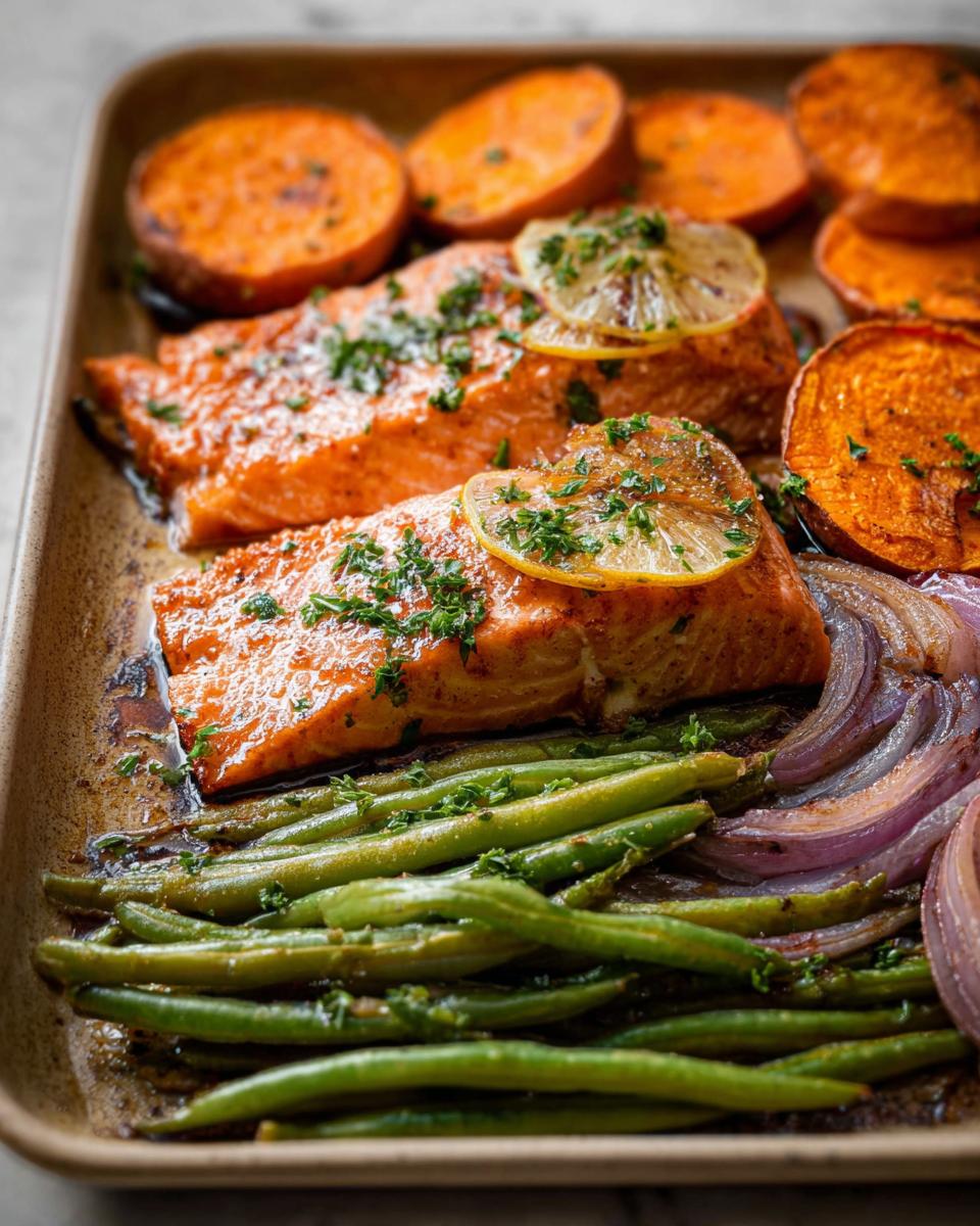 Close-up of a sheet pan with baked salmon fillets, roasted sweet potato slices, green beans, and red onion wedges, perfect for salmon recipes meal prep.
