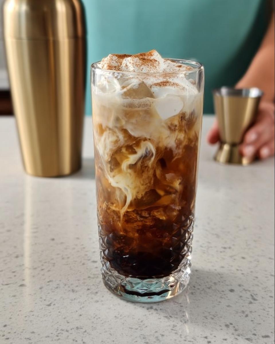 A tall glass of iced coffee with swirls of cream and a dusting of cinnamon, part of Starbucks Drinks Recipes.