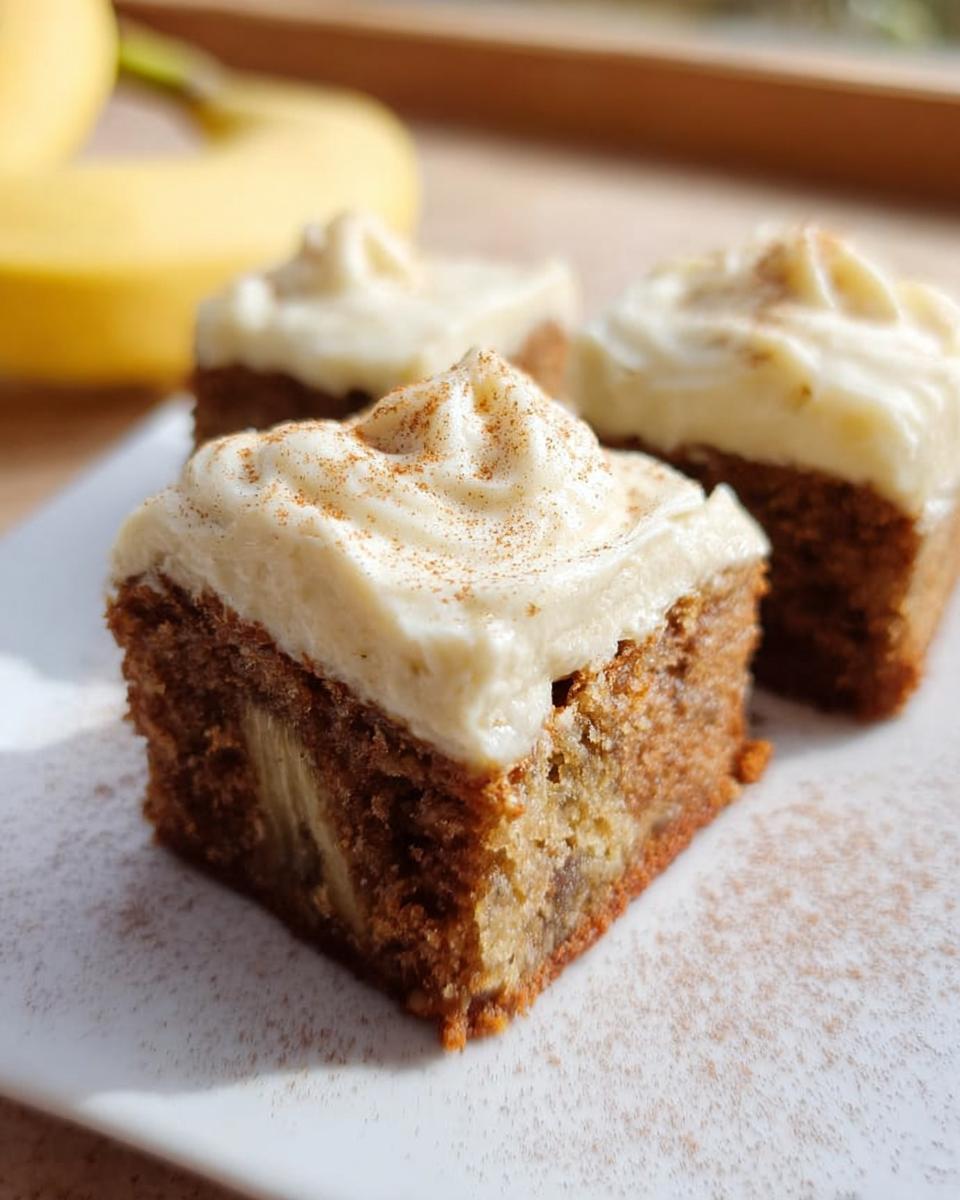 Close-up of three Banana Bread Brownies Made Easy, topped with swirled cream cheese frosting and a sprinkle of cinnamon.