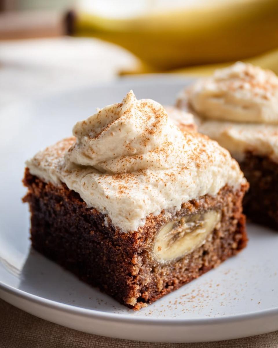 A slice of Banana Bread Brownies Made Easy, topped with creamy frosting and a sprinkle of cinnamon, with a banana slice inside.