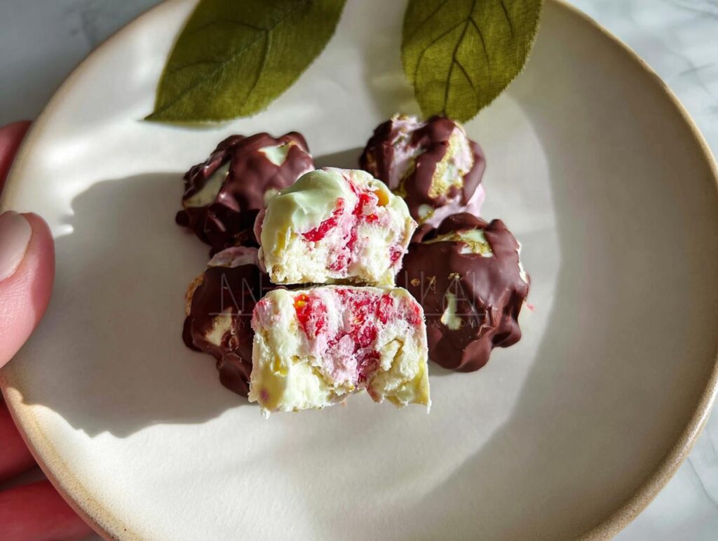 Close-up of chocolate strawberry yogurt clusters, showing the creamy white yogurt center with pink strawberry pieces and a dark chocolate coating.