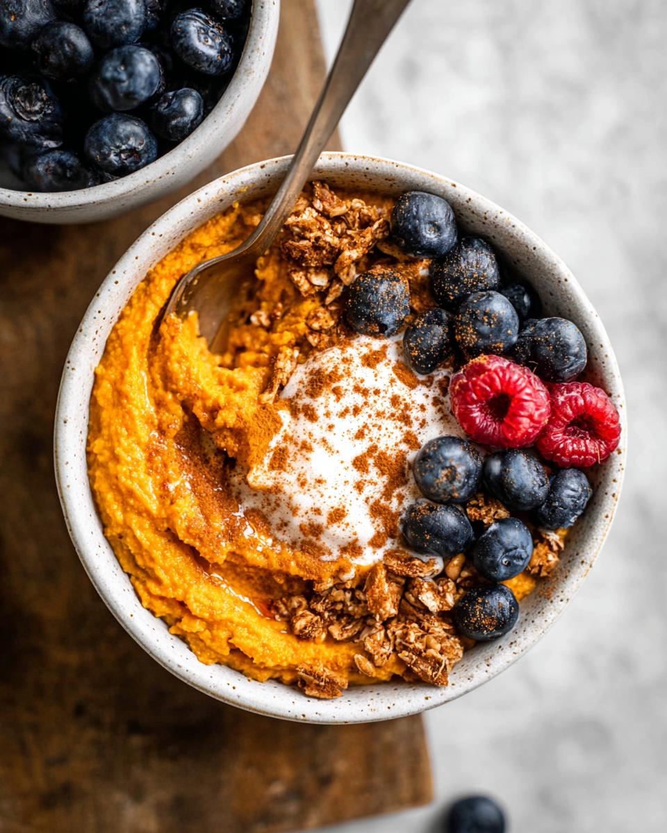 A Delicious Sweet Potato Breakfast Bowl topped with yogurt, blueberries, raspberries, granola, and cinnamon.