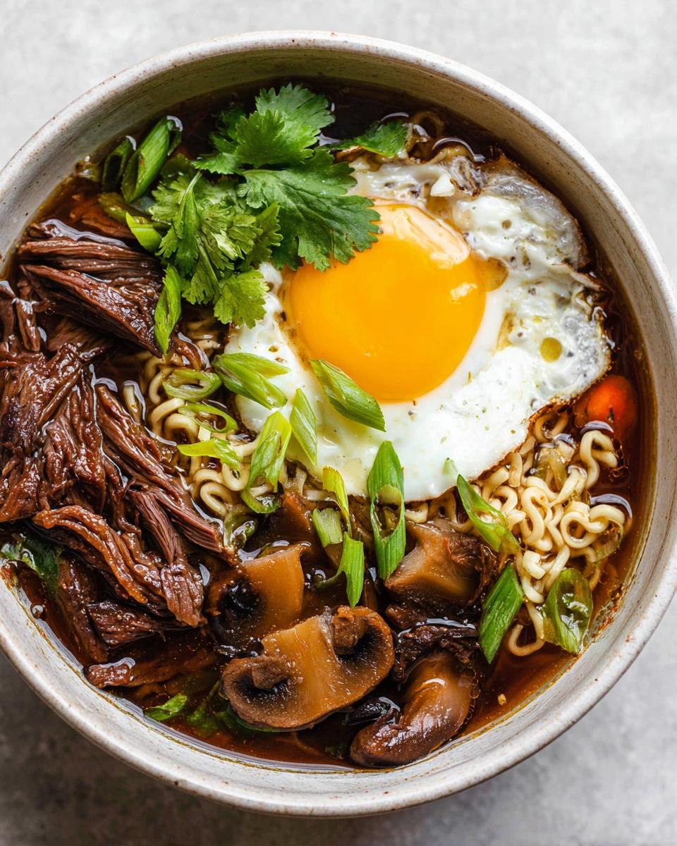 A close-up of a bowl of Slow Cooker Beef Ramen Noodles topped with a fried egg, mushrooms, and green onions.
