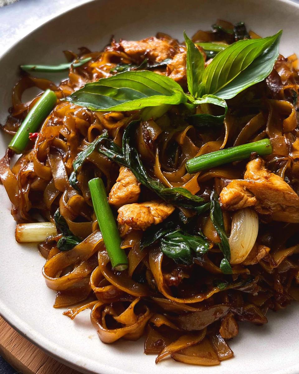 Close-up of delicious Street Style Thai Drunken Noodles with tender chicken pieces and fresh basil.