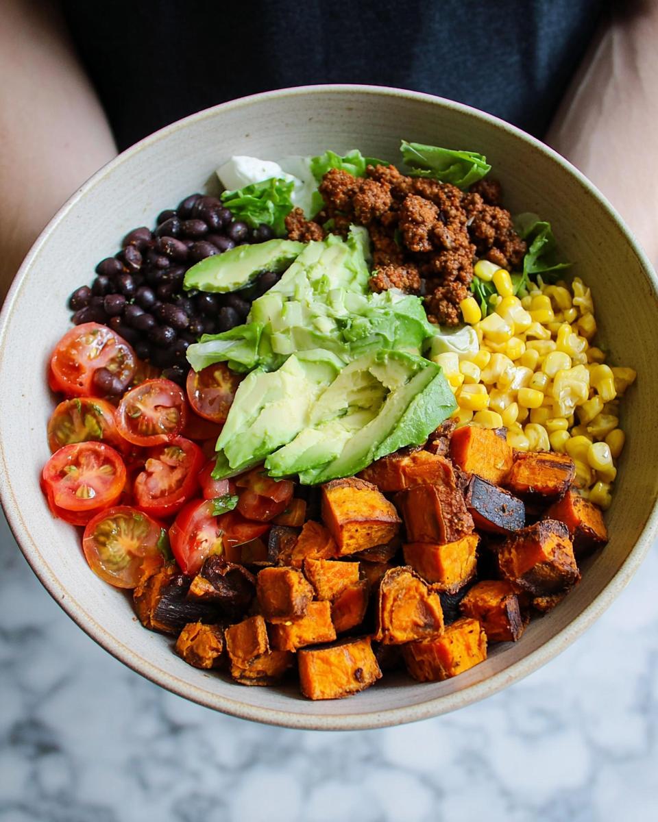 A vibrant Sweet Potato Taco Bowl filled with roasted sweet potatoes, black beans, corn, avocado, tomatoes, and seasoned ground meat.