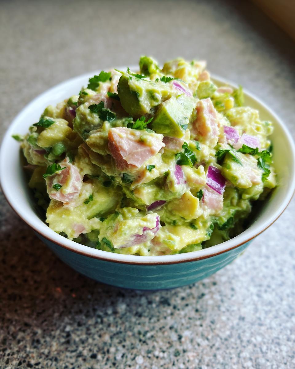 Close-up of a bowl filled with creamy avocado tuna salad, featuring chunks of avocado, tuna, red onion, and parsley.