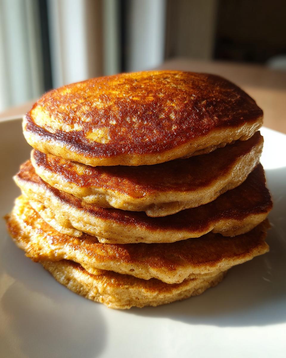 A stack of golden-brown banana oat pancakes on a white plate, ready for breakfast.