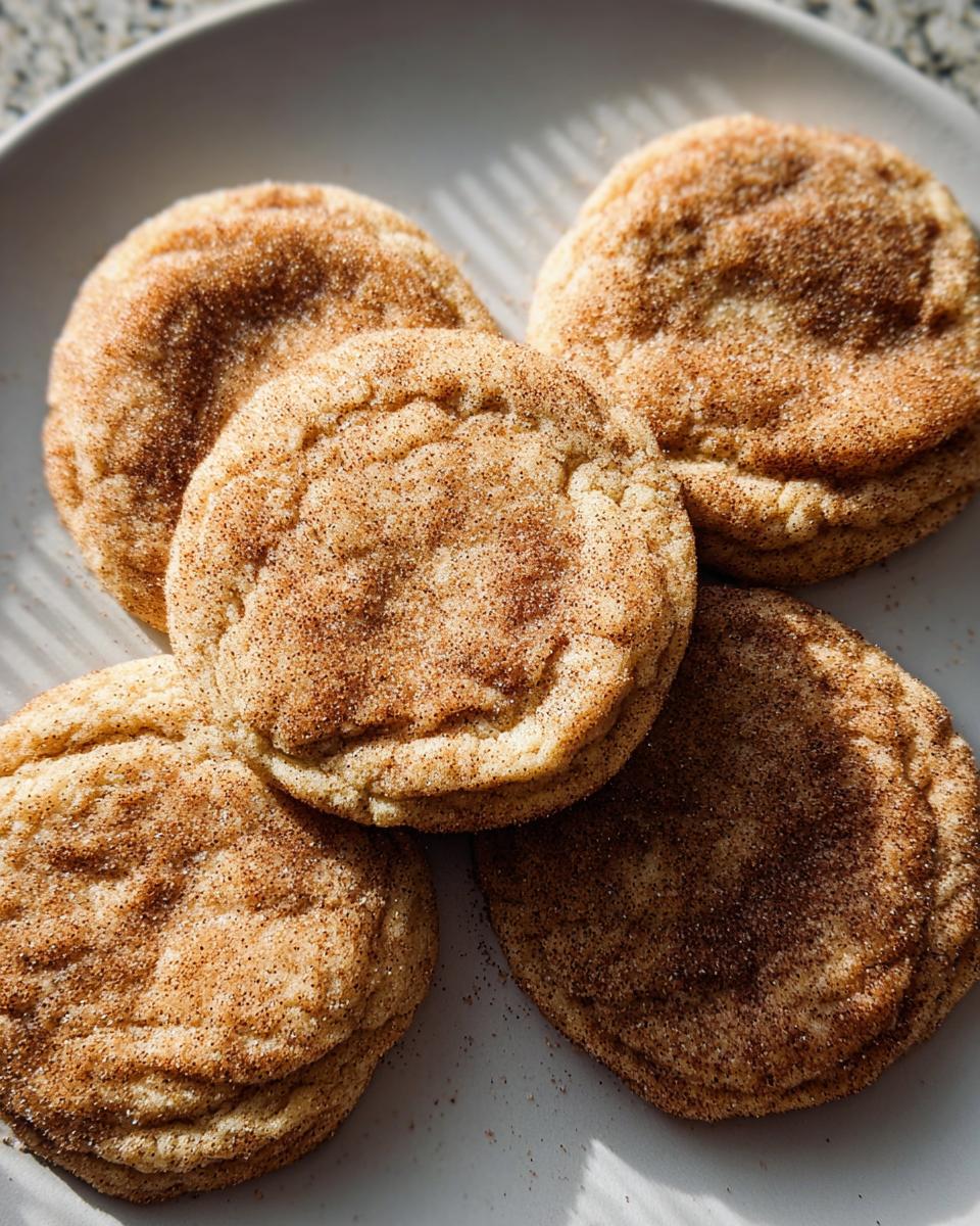 A close-up of five Chewy Churro Cookies, dusted with cinnamon sugar, piled on a light gray plate.