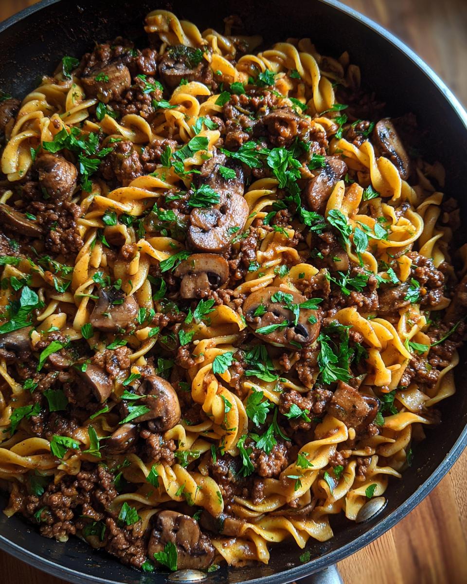 Close-up of a creamy beef stroganoff skillet meal with fusilli pasta, ground beef, mushrooms, and parsley.