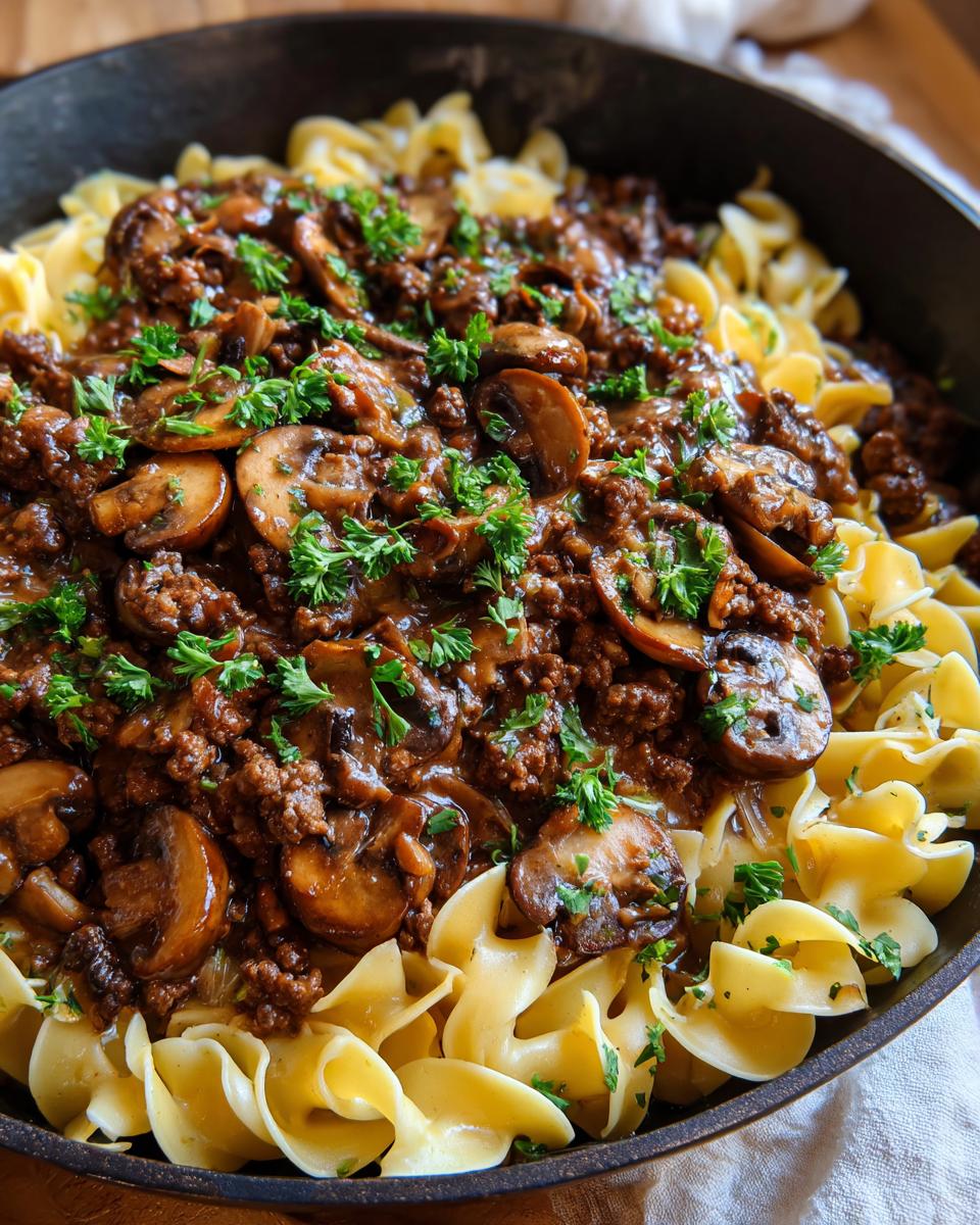 Close-up of a creamy beef stroganoff skillet meal with ground beef, mushrooms, and egg noodles, garnished with parsley.