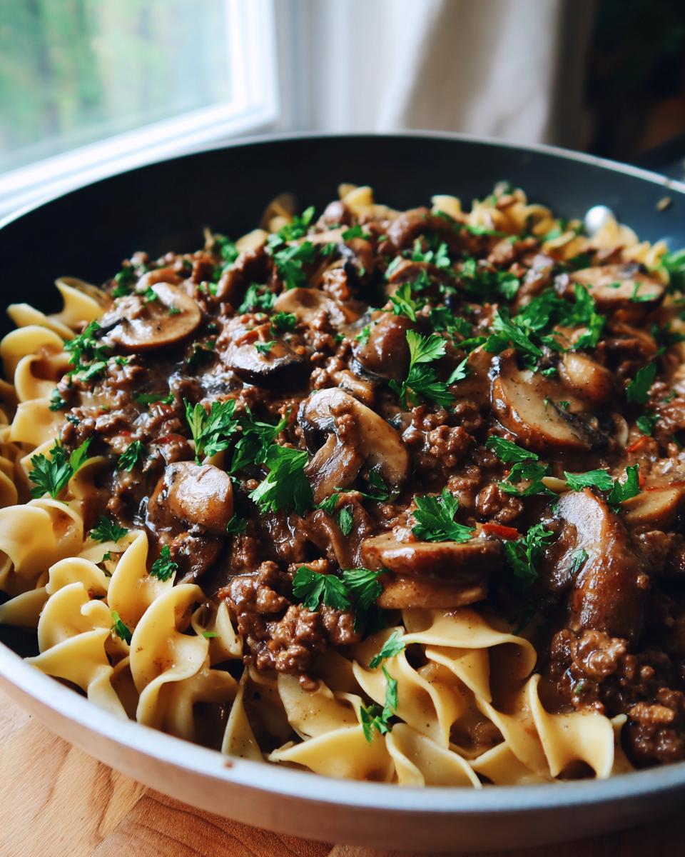 A close-up of a creamy beef stroganoff skillet meal with ground beef, mushrooms, and egg noodles, garnished with parsley.