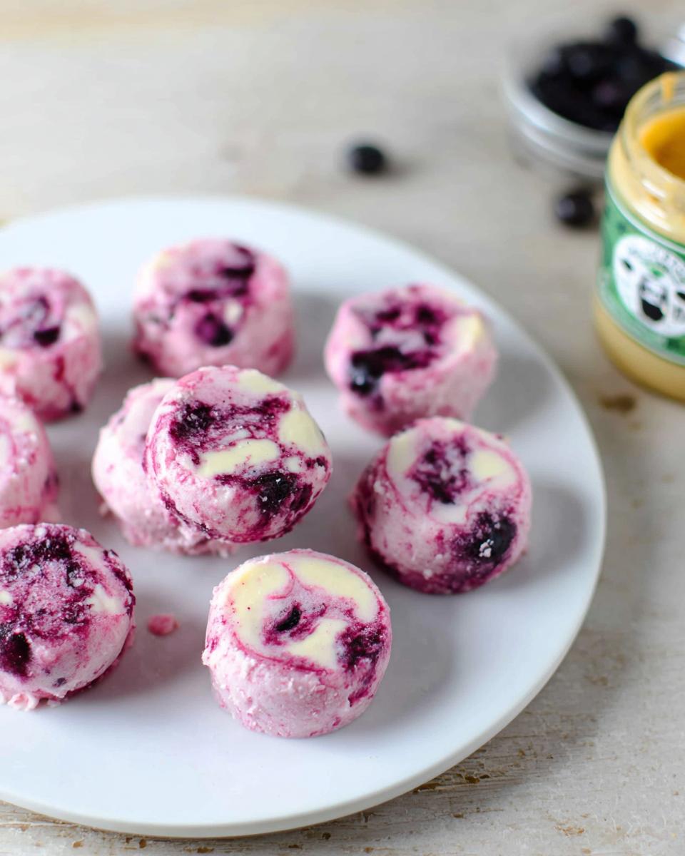 A plate of round, pink blueberry swirl yogurt bites with swirls of white yogurt and blueberries.