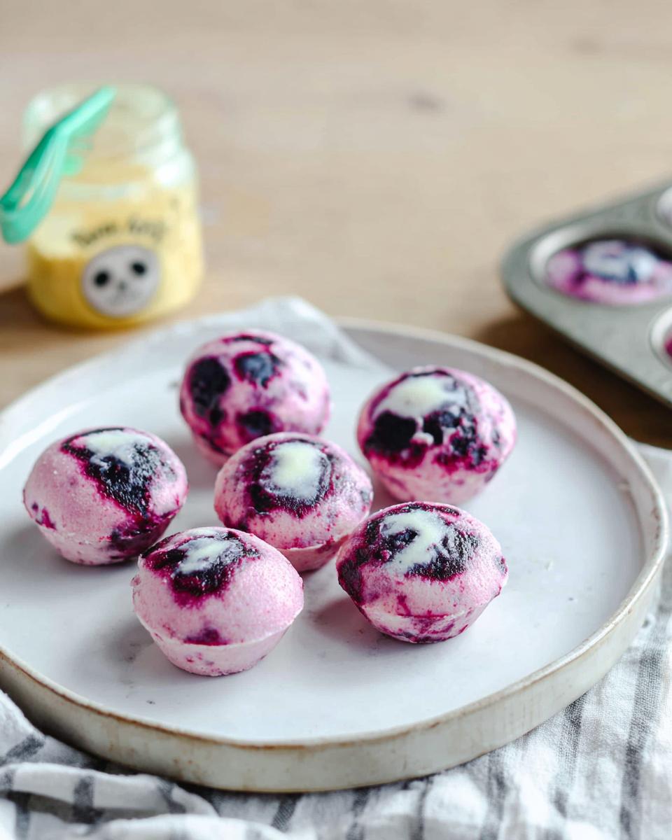 Six Easy Blueberry Swirl Yogurt Bites on a white plate, with a muffin tin in the background.
