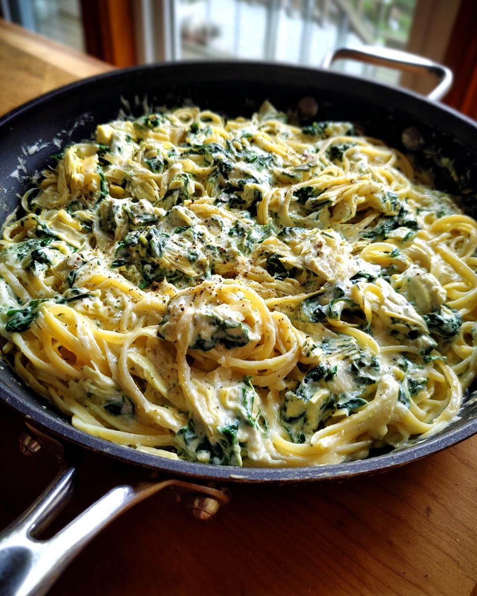 A close-up of creamy spinach artichoke pasta in a skillet, showcasing the pasta, spinach, and artichoke hearts in a rich sauce.
