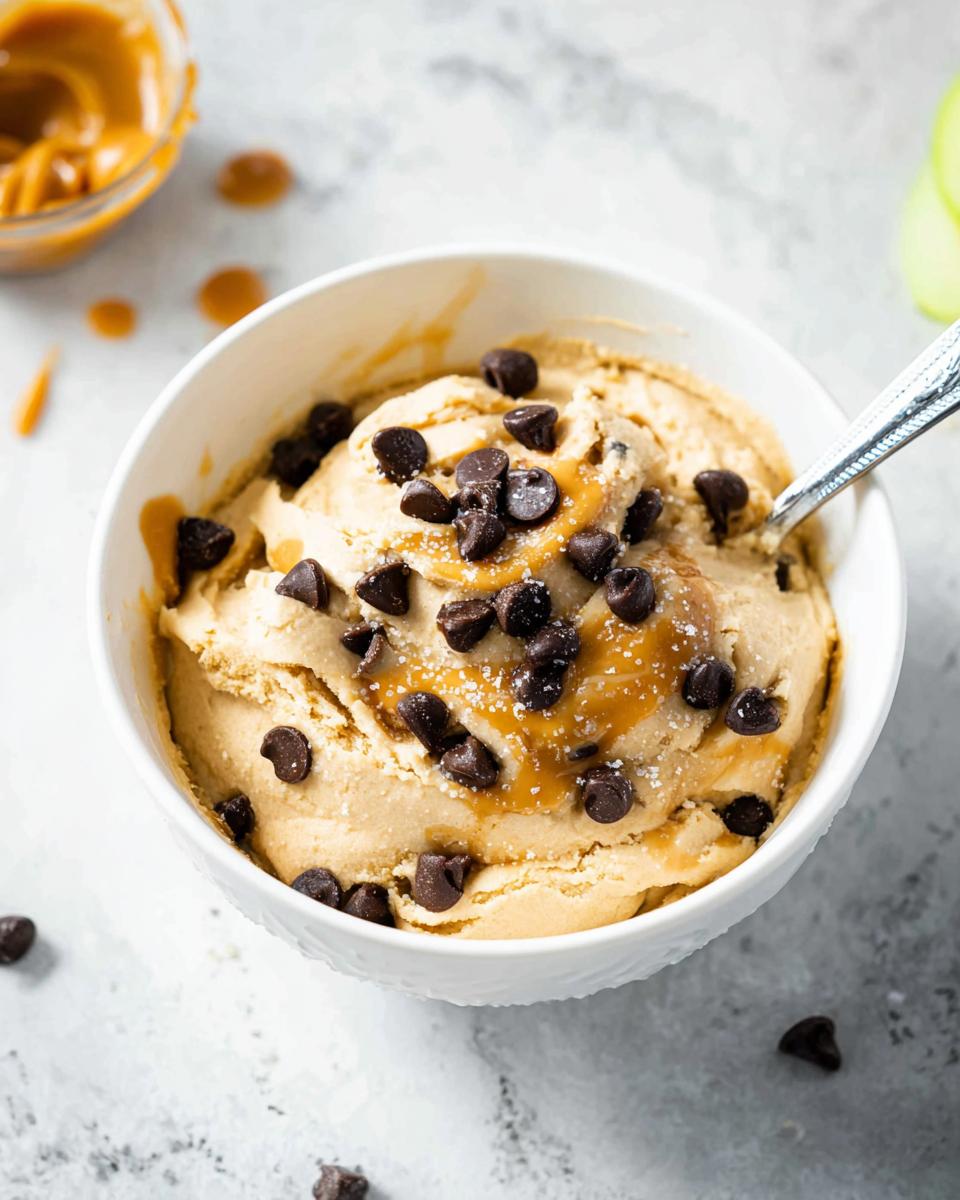 A bowl of Greek Yogurt Cookie Dough topped with chocolate chips and caramel drizzle.