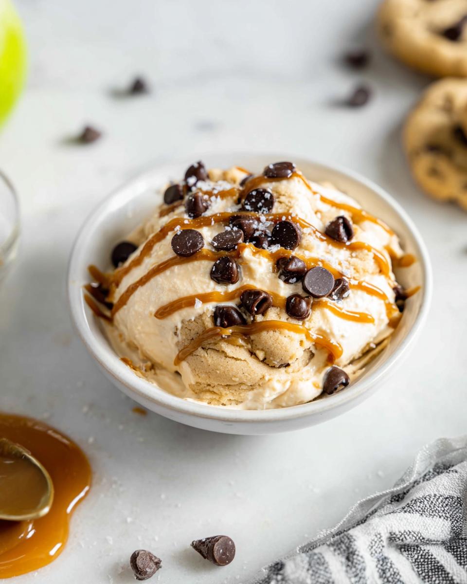 A bowl of Greek yogurt cookie dough ice cream topped with chocolate chips and caramel drizzle.