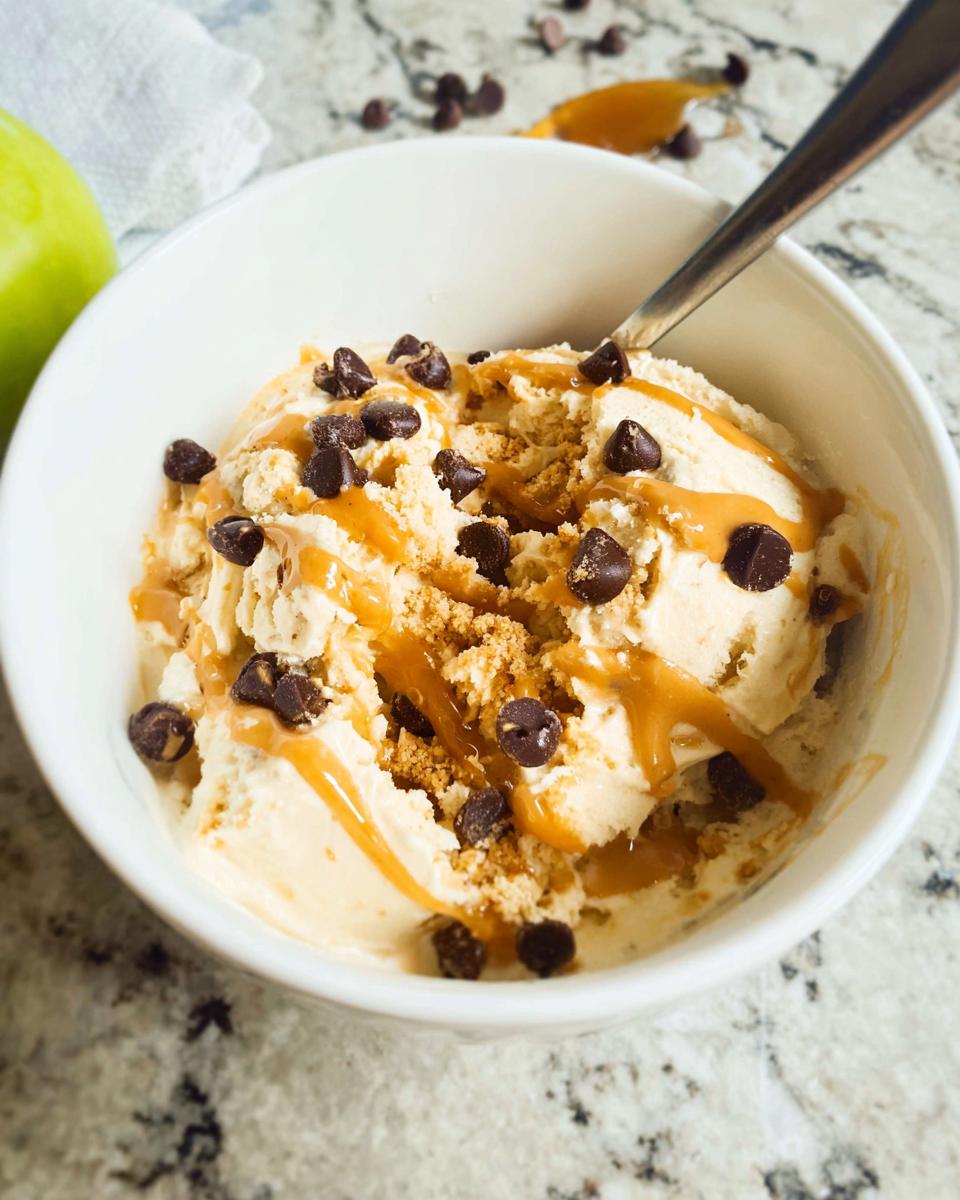 A bowl of Greek Yogurt Cookie Dough ice cream topped with chocolate chips and caramel sauce.