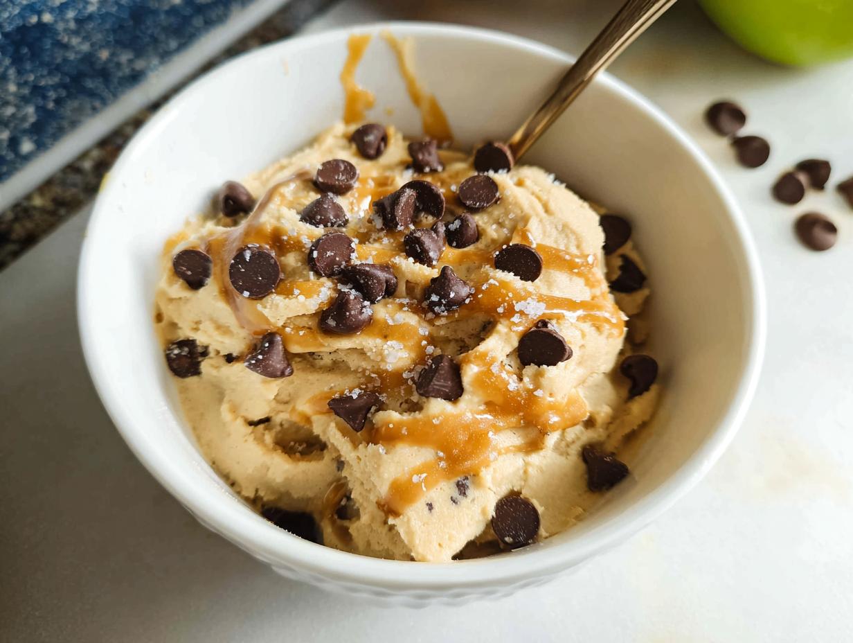 A bowl of Greek Yogurt Cookie Dough ice cream topped with chocolate chips and caramel drizzle.