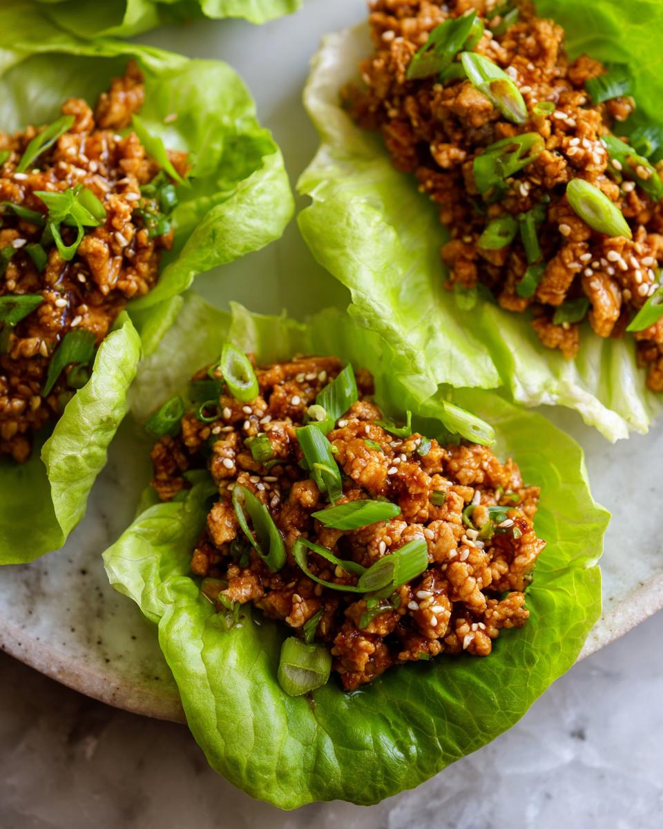 Close-up of healthy chicken lettuce wraps filled with seasoned ground chicken and topped with green onions and sesame seeds.