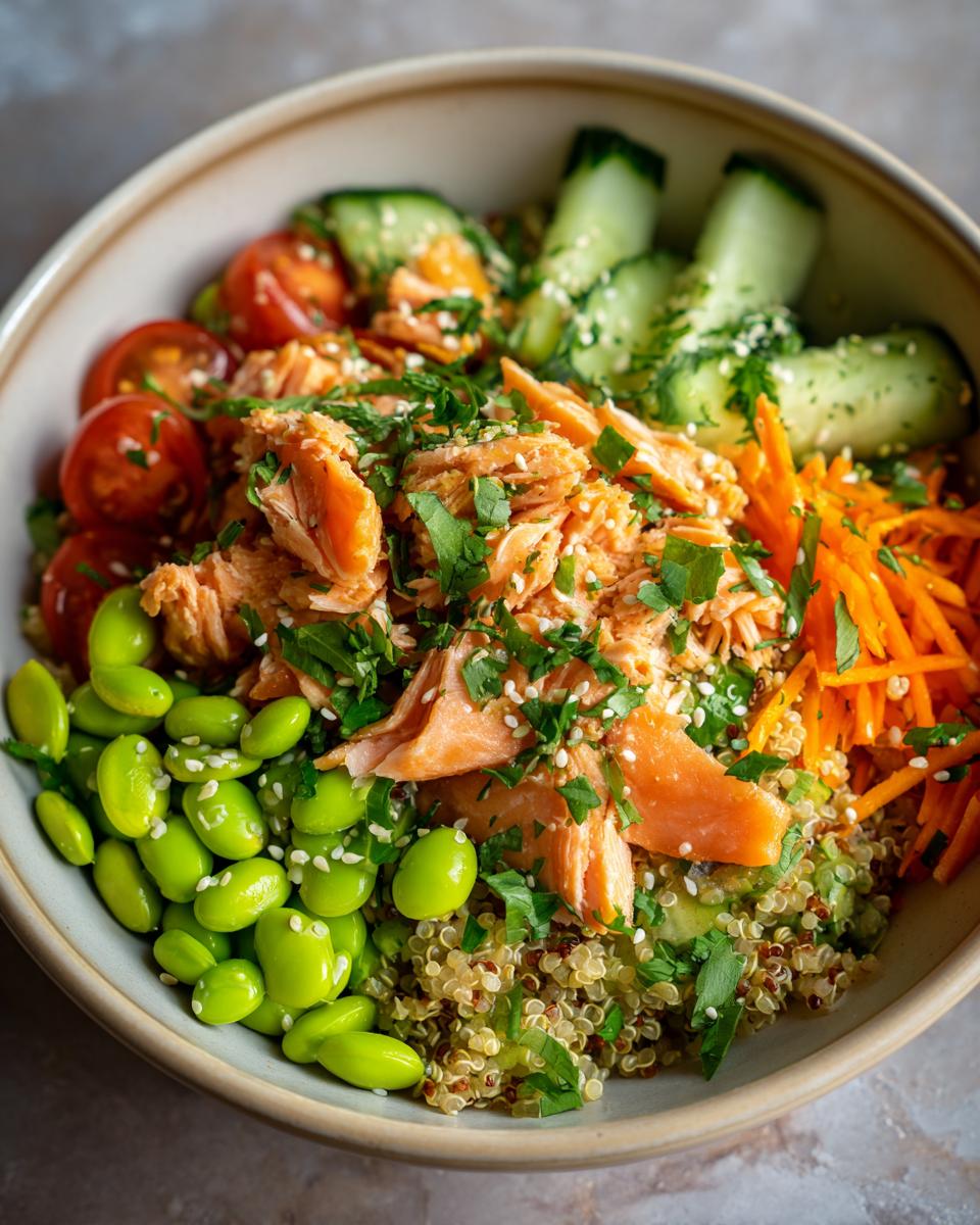 A vibrant and healthy salmon power bowl featuring flaked salmon, quinoa, edamame, cherry tomatoes, cucumber, and shredded carrots.