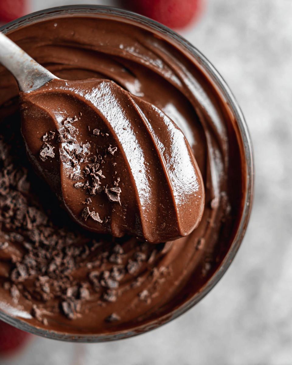 A close-up shot of a spoon scooping rich High Protein Chocolate Pudding, sprinkled with chocolate shavings.