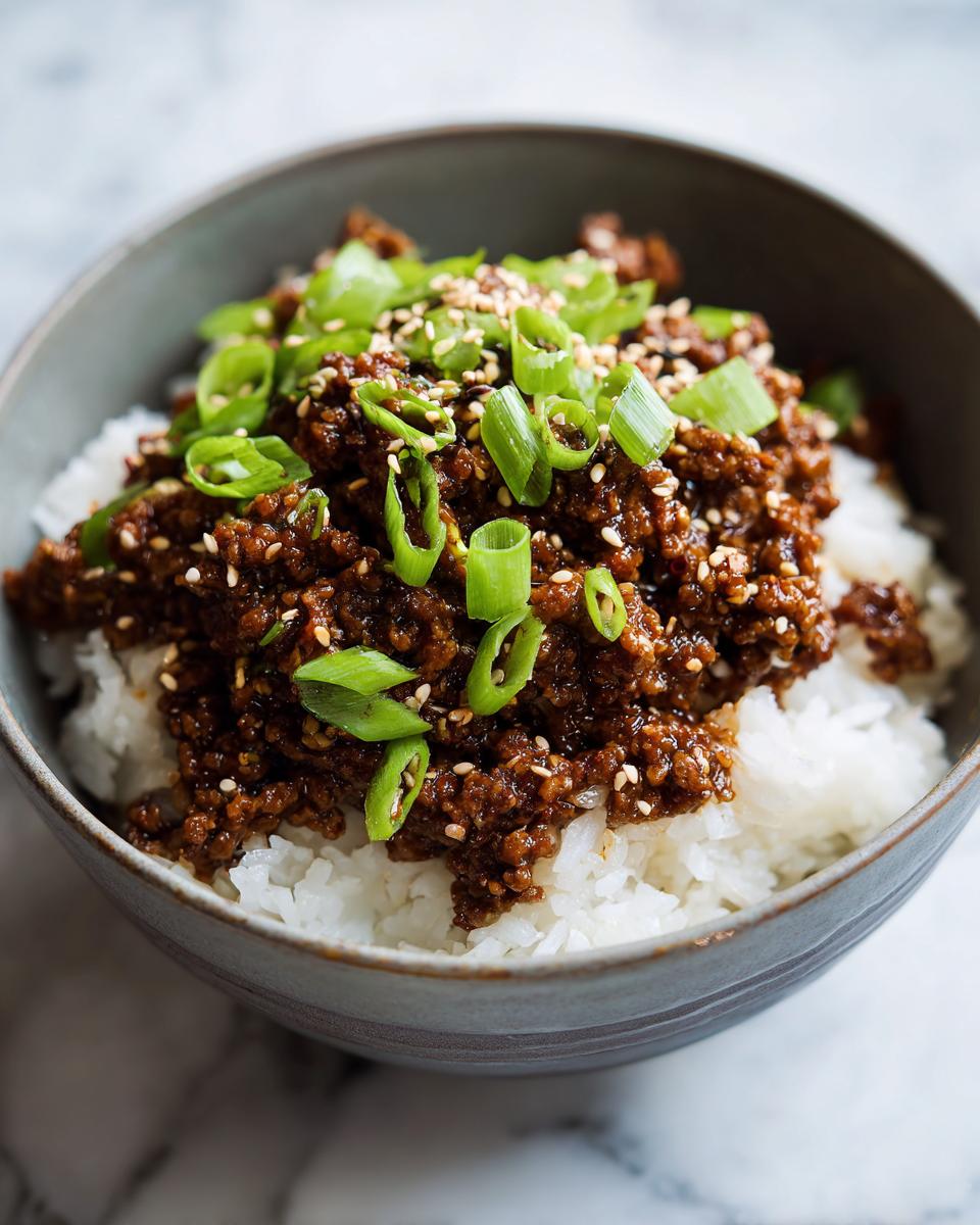 Close-up of a Korean beef rice bowl topped with sesame seeds and chopped green onions.