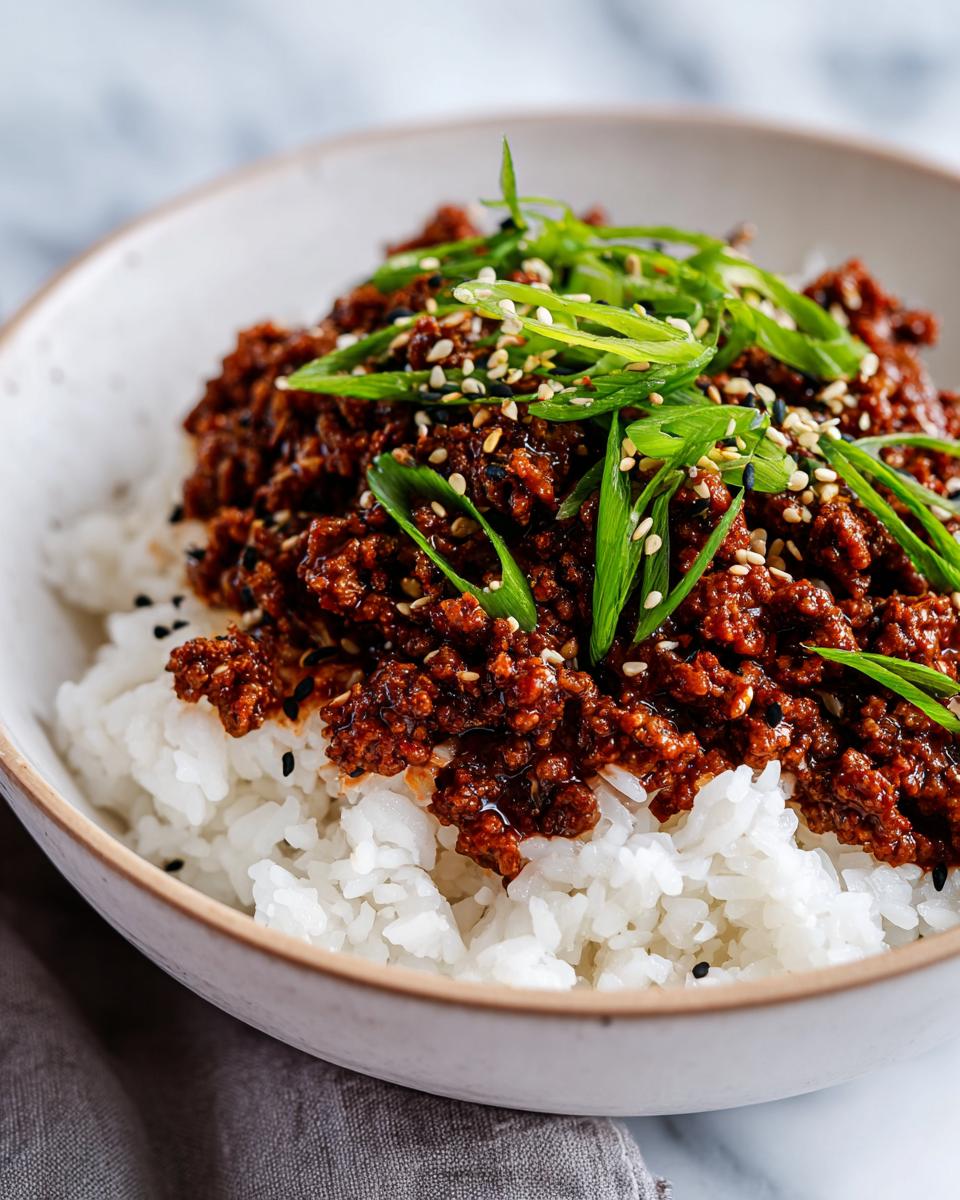 Close-up of a Korean beef rice bowl with seasoned ground beef, white rice, sesame seeds, and green onions.