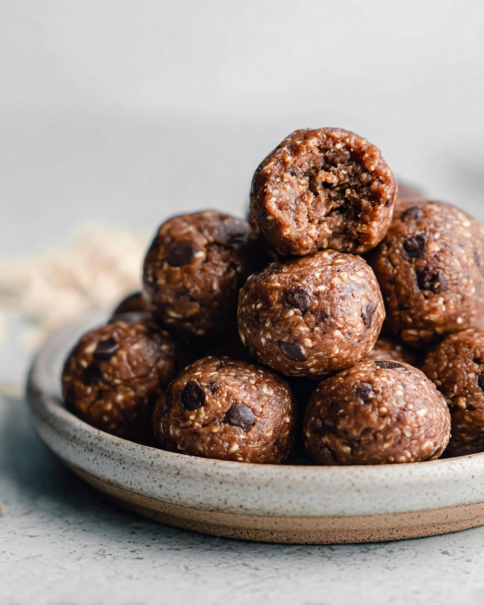 A pile of No-Bake Chocolate Peanut Butter Protein Balls in a bowl, one is bitten into.