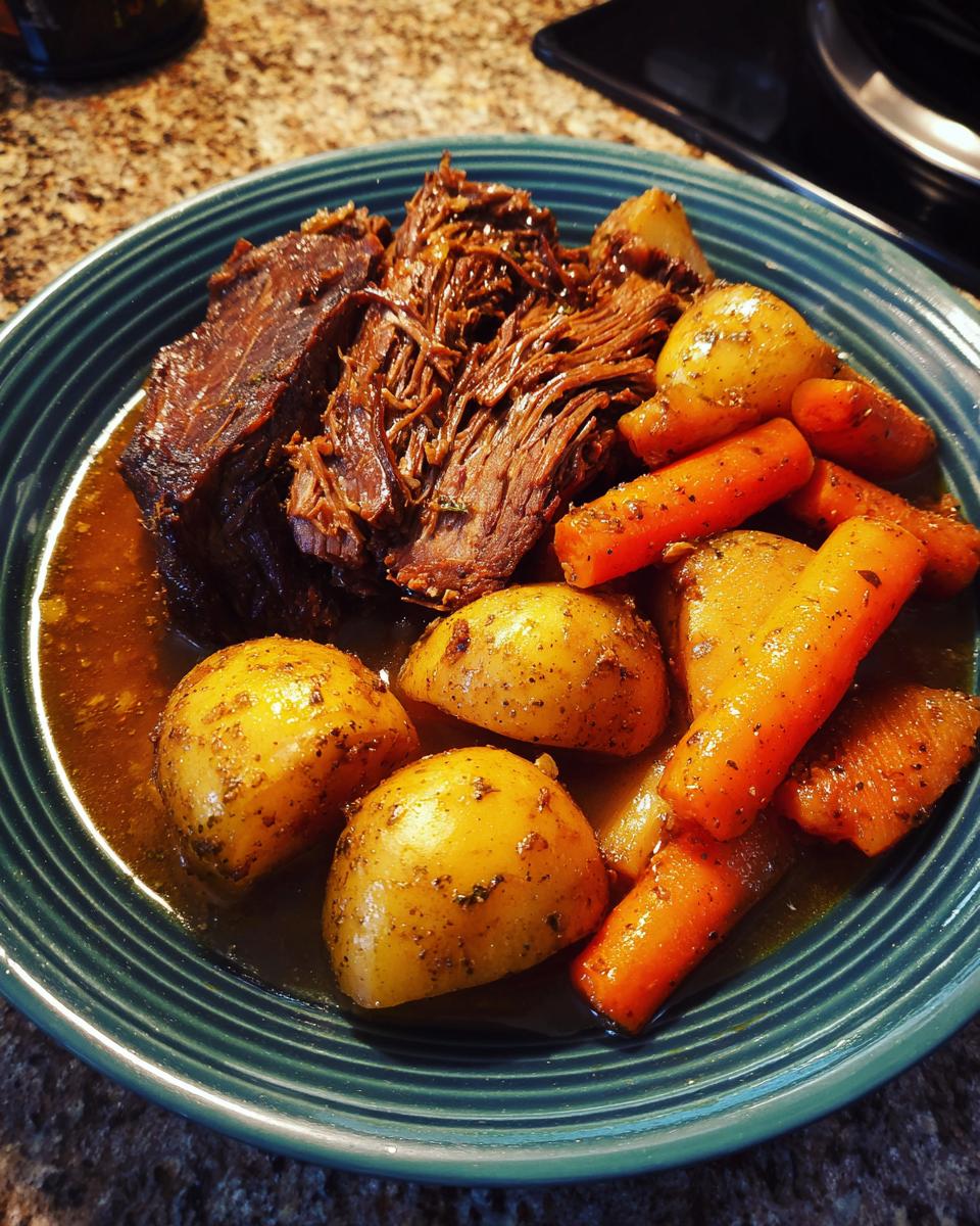 A plate of tender pot roast with fork-tender shredded beef, alongside roasted carrots and potatoes, in a rich gravy.